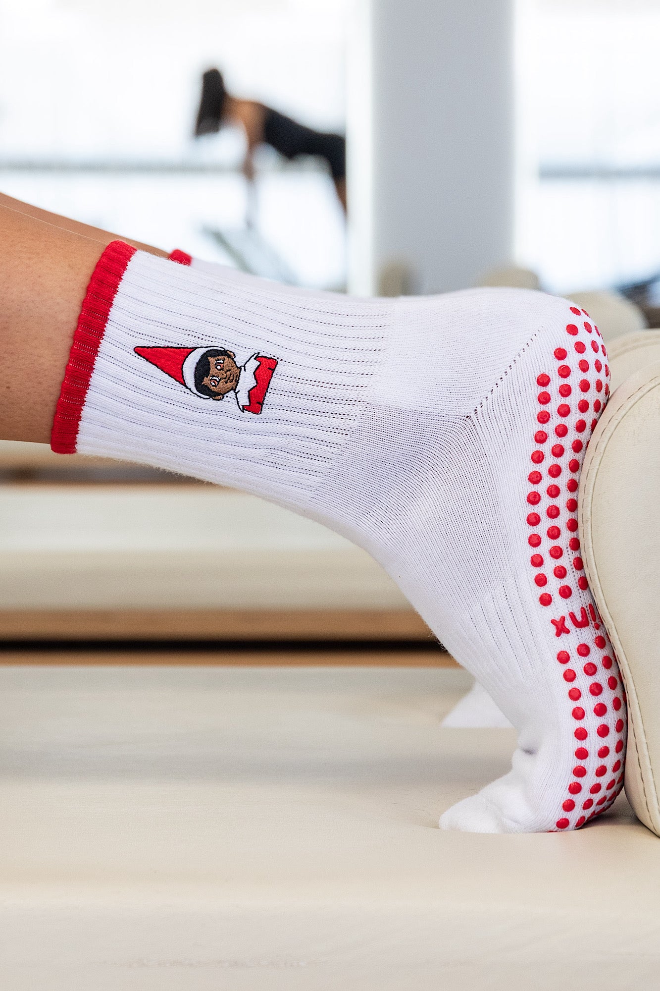 White grip socks sock with red The Elf On The Shelf On a reformer bed doing Pilates for Christmas