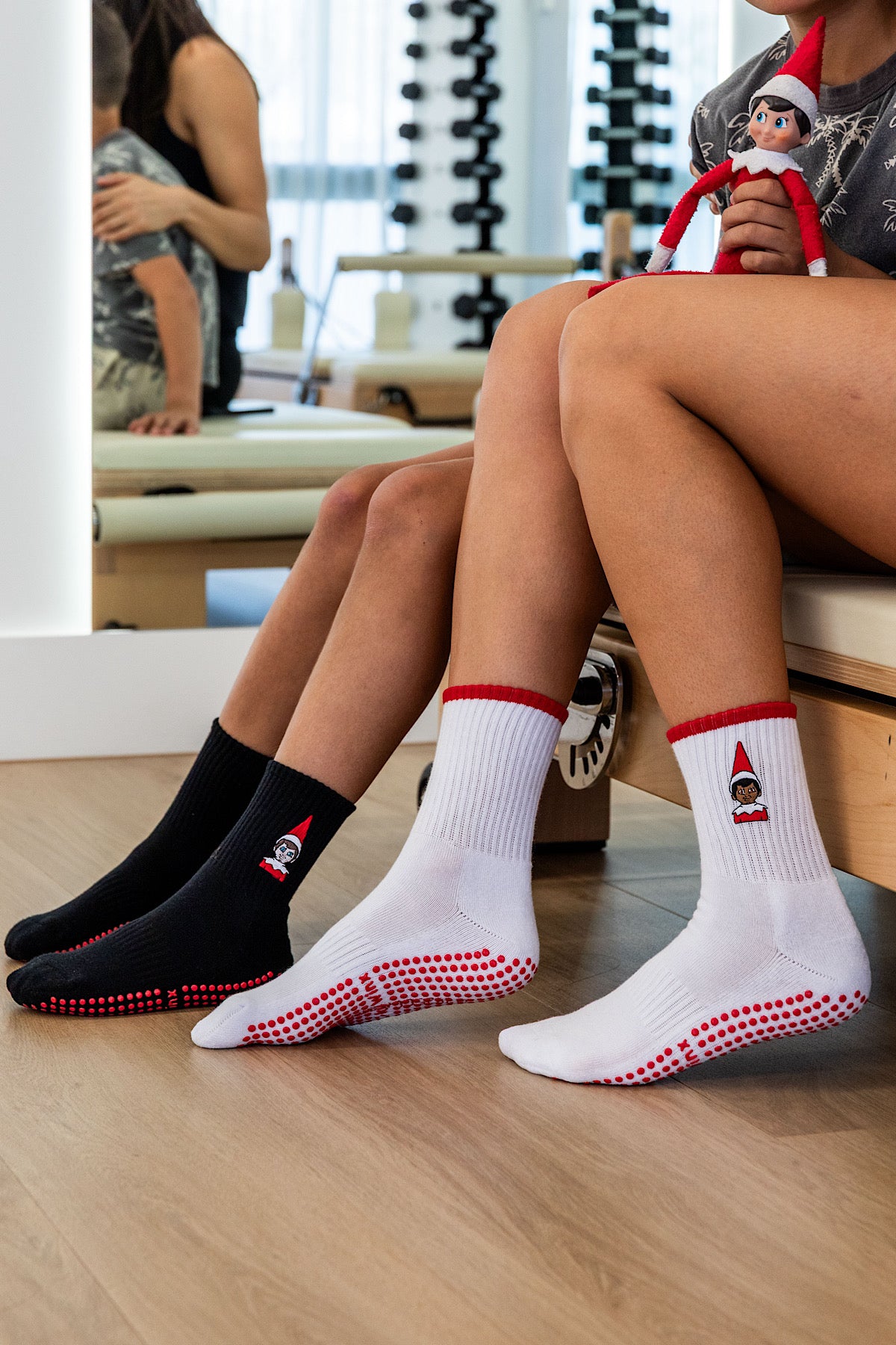 Two pairs of Christmas The Elf On The Shelf Pilates and reformer grip socks with non-slip sole design on a wooden floor 