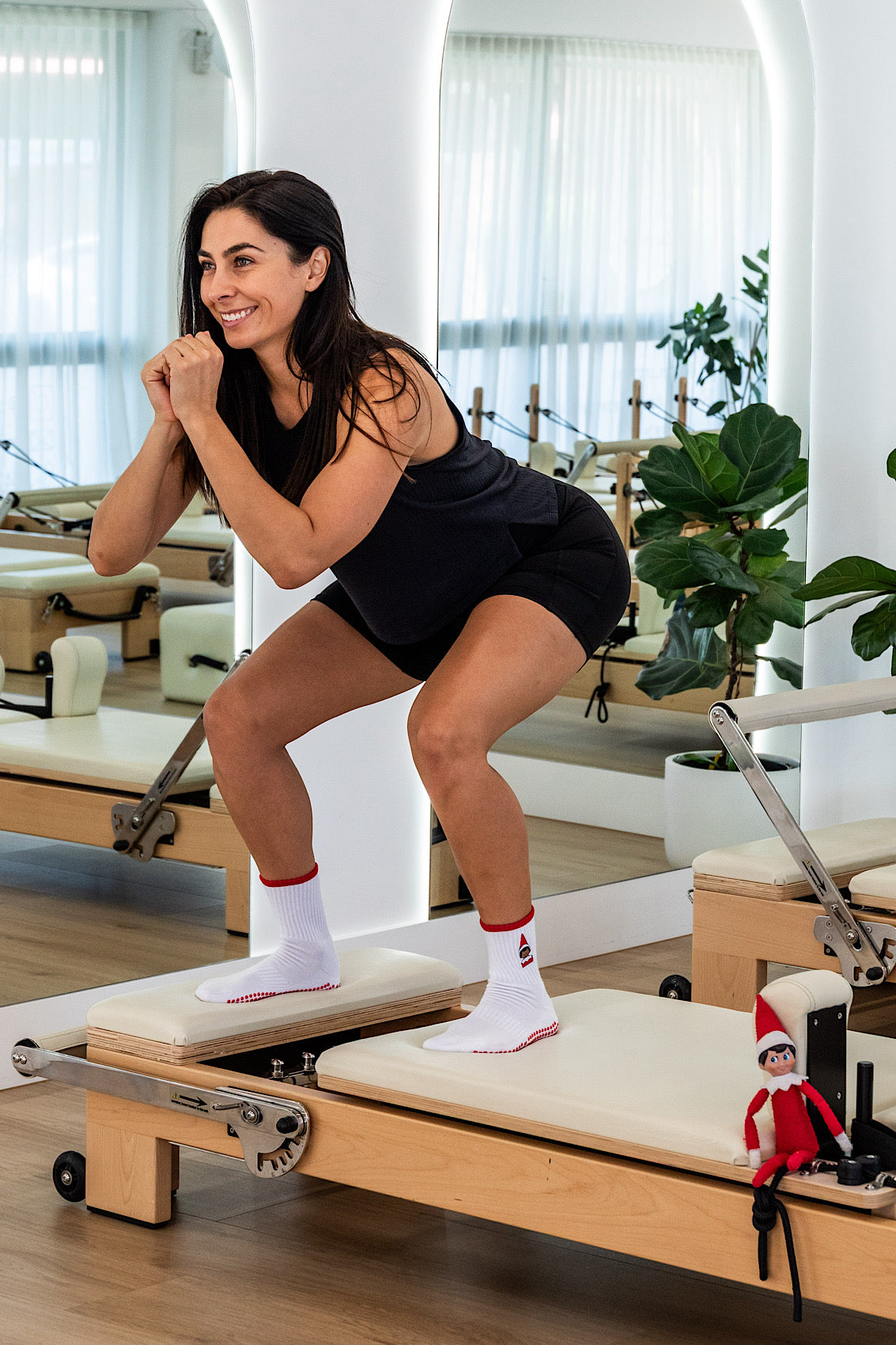 Woman exercising on a Pilates reformer machine in a studio setting wearing The Elf On The Shelf Grip socks